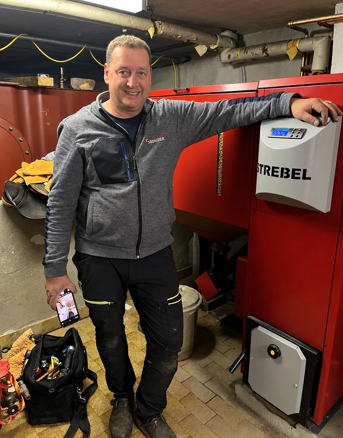 Jürgen Benzer in Arbeitskleidung neben einer Heizungsanlage